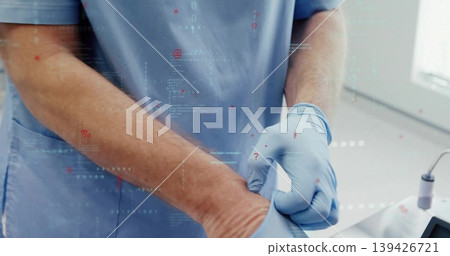 Male healthcare worker pulling blue glove onto hand in exam room, with scrubs, sink, data symbols Male healthcare worker pulling blue glove onto hand in exam room, with scrubs, sink, data symbols 139426721