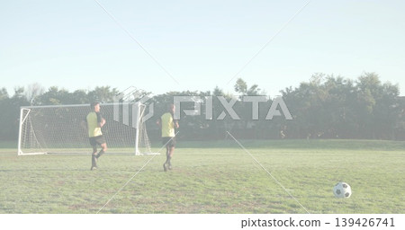 Jogging players wearing training vests, black shorts on park field, with portable goal, soccer ball 139426741