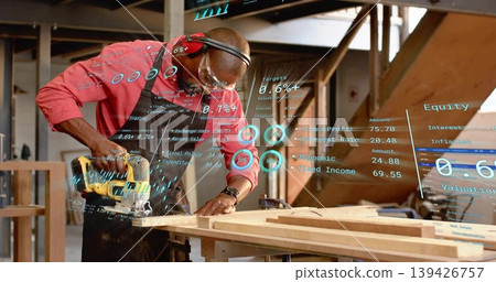 Carpenter wearing safety gear cutting wooden plank with circular saw in workshop with digital data Carpenter wearing safety gear cutting wooden plank with circular saw in workshop with digital data 139426757