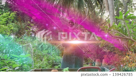 Standing Black gardener inspecting clay pot at bench in tropical garden, with teal light streaks Standing Black gardener inspecting clay pot at bench in tropical garden, with teal light streaks 139426785