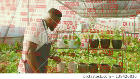 Leaning man wearing apron checking seedling pot on metal shelving in greenhouse, with binary code Leaning man wearing apron checking seedling pot on metal shelving in greenhouse, with binary code 139426836