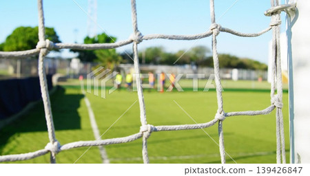 Framing white knotted goal net and right goalpost at club soccer pitch, players wearing bright bibs 139426847