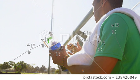 Sitting athlete in green shirt with towel holding bottle on bleachers beside field, HUD, copy space 139426849