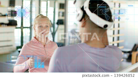 Holding small weight, woman in pink top coaching partner with VR headset at gym, AR graphics Holding small weight, woman in pink top coaching partner with VR headset at gym, AR graphics 139426852