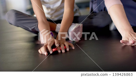 Reaching child wearing striped top dark leggings on studio mat, adult reaching toward small red toy Reaching child wearing striped top dark leggings on studio mat, adult reaching toward small red toy 139426863