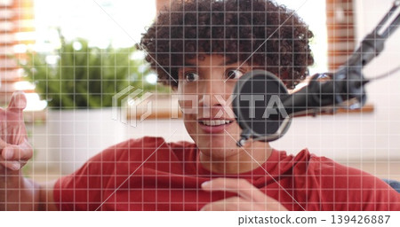 Reacting male creator leaning toward black mic in home studio with grid overlay, wearing red tee Reacting male creator leaning toward black mic in home studio with grid overlay, wearing red tee 139426887