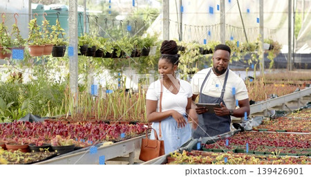 Guiding customer white skirt with brown handbag, staff in apron holding tablet, nursery blue labels Guiding customer white skirt with brown handbag, staff in apron holding tablet, nursery blue labels 139426901