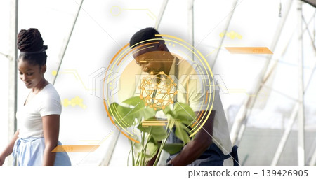 Inspecting mid adult man wearing denim apron leaning over potted plants in greenhouse, AR overlays 139426905
