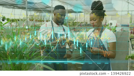 Reviewing tablet two nursery workers examining data overlay amid potted plants, wearing dark aprons Reviewing tablet two nursery workers examining data overlay amid potted plants, wearing dark aprons 139426922