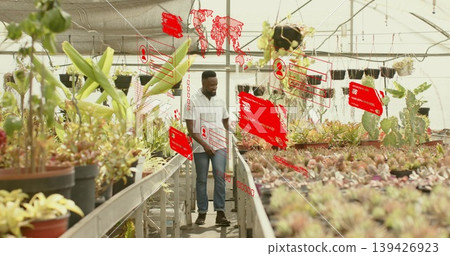 Walking man in striped shirt and jeans examining plants in greenhouse, with AR data overlays 139426923