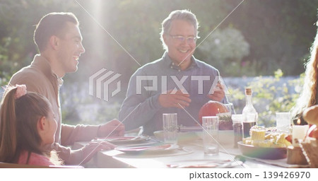 Holding pumpkin, man at center wearing sweater carving with utensil at garden patio dining table Holding pumpkin, man at center wearing sweater carving with utensil at garden patio dining table 139426970