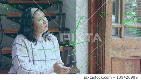 Holding smartphone, mature woman gazing toward light by wooden doorway, in checked sweater, overlay 139426999