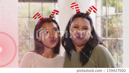 Posing two women standing close together at home, wearing knit sweaters and candy-cane headbands Posing two women standing close together at home, wearing knit sweaters and candy-cane headbands 139427002