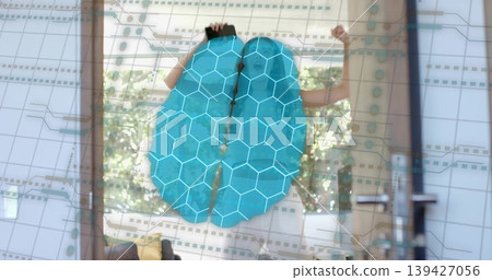 Standing adult woman in pale outfit at home touching phone and gesturing at blue brain hologram Standing adult woman in pale outfit at home touching phone and gesturing at blue brain hologram 139427056