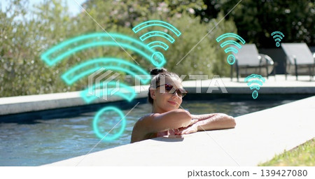 Leaning woman resting on concrete coping at pool deck in dark sunglasses, swimsuit, turquoise Wi?Fi 139427080