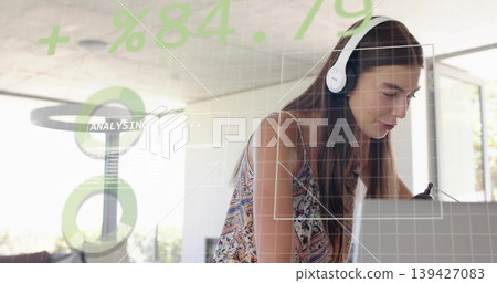 Leaning woman wearing patterned top and white headset typing on laptop in home office HUD overlays Leaning woman wearing patterned top and white headset typing on laptop in home office HUD overlays 139427083