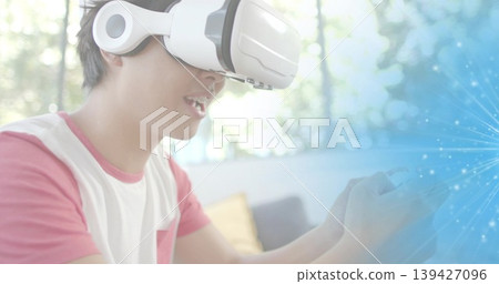 Using white VR headset with headphones, man wearing pink sleeves T-shirt on couch with blue overlay Using white VR headset with headphones, man wearing pink sleeves T-shirt on couch with blue overlay 139427096