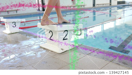 Standing female swimmer in racing suit adjusting stance on block 2 at pool, with paint overlays Standing female swimmer in racing suit adjusting stance on block 2 at pool, with paint overlays 139427145