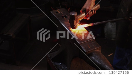 Striking smith hands wearing dark shirt with tongs, hammer on anvil at forge, hitting glowing rod Striking smith hands wearing dark shirt with tongs, hammer on anvil at forge, hitting glowing rod 139427166