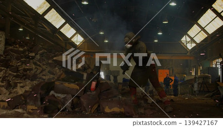 Striking worker wearing helmet mask apron gloves boots prying rubble at warehouse, handheld tool Striking worker wearing helmet mask apron gloves boots prying rubble at warehouse, handheld tool 139427167