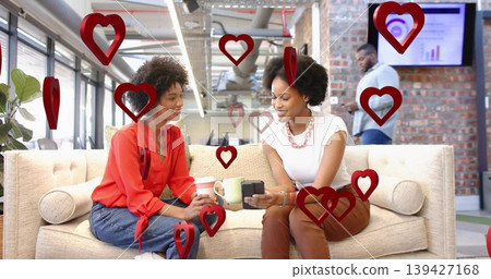Chatting pair wearing red blouse and white top holding coffee, device on office sofa, red hearts Chatting pair wearing red blouse and white top holding coffee, device on office sofa, red hearts 139427168