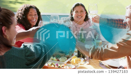 Clinking glasses six diners in casual clothes leaning around backyard table with yellow tablecloth Clinking glasses six diners in casual clothes leaning around backyard table with yellow tablecloth 139427183