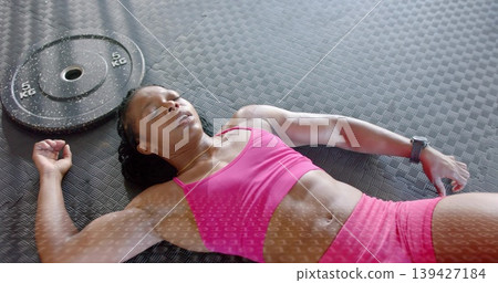 Lying adult woman wearing pink sportswear on textured mat, with 5-kg plate, smartwatch, gold chain Lying adult woman wearing pink sportswear on textured mat, with 5-kg plate, smartwatch, gold chain 139427184