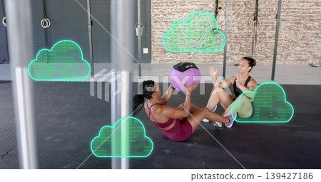 Passing purple 10LB medball, two women in sportswear bracing feet on gym floor with green overlays Passing purple 10LB medball, two women in sportswear bracing feet on gym floor with green overlays 139427186