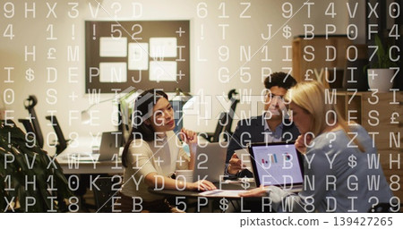 Collaborating three colleagues in office attire at table showing laptop chart, with data overlay 139427265