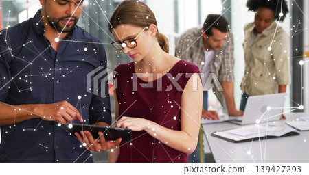 Holding tablet, woman in maroon top pointing at screen in office with laptop and network overlay Holding tablet, woman in maroon top pointing at screen in office with laptop and network overlay 139427293