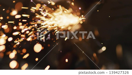 Streaming orange-yellow sparks across dark bench making embers, bokeh, smoke, source off-frame Streaming orange-yellow sparks across dark bench making embers, bokeh, smoke, source off-frame 139427326