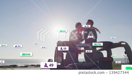 Sitting two men in striped tank embracing, watching horizon on SUV rear at beach, floating icons 139427344