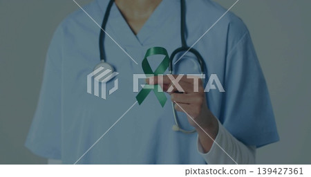 Holding green awareness ribbon, nurse wearing scrubs and undershirt at clinic, with stethoscope Holding green awareness ribbon, nurse wearing scrubs and undershirt at clinic, with stethoscope 139427361