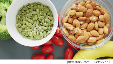 Displaying two bowls of pepitas and almonds on dark gray counter with tomatoes, banana, broccoli Displaying two bowls of pepitas and almonds on dark gray counter with tomatoes, banana, broccoli 139427367