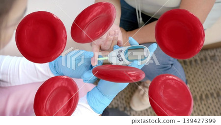 Testing caregiver blue gloves checking fingertip at home, with glucometer and red blood cells Testing caregiver blue gloves checking fingertip at home, with glucometer and red blood cells 139427399