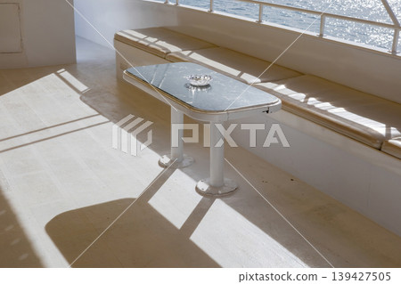 Serene boat deck with sunlit table and cushions overlooking tranquil water Serene boat deck with sunlit table and cushions overlooking tranquil water 139427505