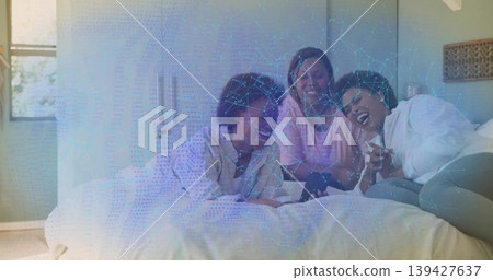Laughing three women wearing loungewear lounging on queen-size bed in bedroom, sharing smartphone Laughing three women wearing loungewear lounging on queen-size bed in bedroom, sharing smartphone 139427637