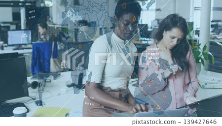 Reviewing two women in business casual leaning over laptop and tablet at office, AR overlay 139427646