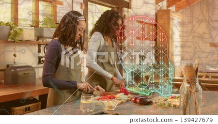Chopping two women wearing olive aprons preparing vegetables on wooden kitchen island, neon overlay 139427679