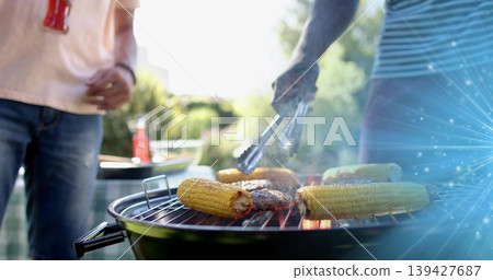 Grilling kettle grill smoking in backyard, with corn, burgers, tongs, men in pink, blue shirts 139427687
