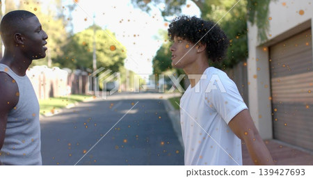 Standing men wearing gray tank top and white T-shirt on suburban street, garage door, orange specks Standing men wearing gray tank top and white T-shirt on suburban street, garage door, orange specks 139427693