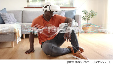 Sitting man wearing white VR headset and orange t-shirt interacting with waveform in living room Sitting man wearing white VR headset and orange t-shirt interacting with waveform in living room 139427704