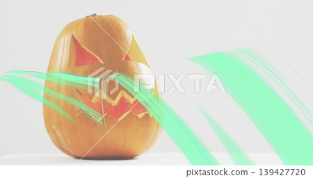 Sitting carved orange pumpkin centered on white tabletop backdrop, showing mint-green streaks 139427720
