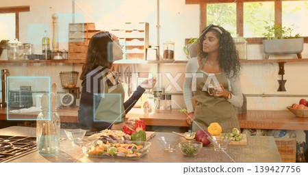Chopping two women wearing aprons preparing vegetables at kitchen island, glass bowls, UI overlays 139427756