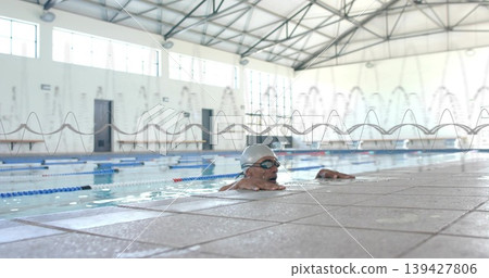Holding pool edge, male swimmer breathing at covered competition pool, wearing goggles and swim cap 139427806