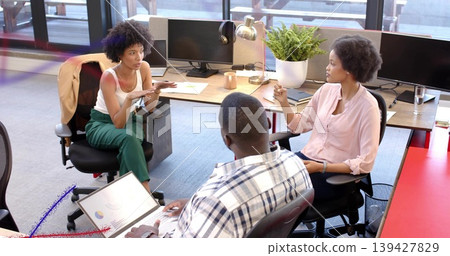 Discussing three colleagues in business casual gesturing in open-plan office, with laptop chart Discussing three colleagues in business casual gesturing in open-plan office, with laptop chart 139427829