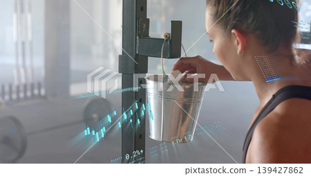 Reaching woman in black tank grabbing chalk from metal bucket at gym, blue charts, copy space Reaching woman in black tank grabbing chalk from metal bucket at gym, blue charts, copy space 139427862