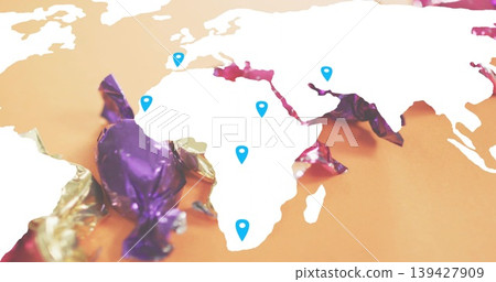 Displaying white map cutout centered on orange tabletop, showing blue pins and purple gold wrappers Displaying white map cutout centered on orange tabletop, showing blue pins and purple gold wrappers 139427909