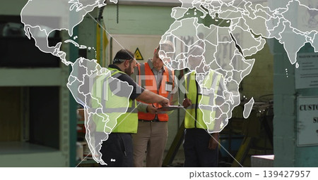 Reviewing clipboard three men in hi-vis vests discussing on factory floor, with world map overlay Reviewing clipboard three men in hi-vis vests discussing on factory floor, with world map overlay 139427957
