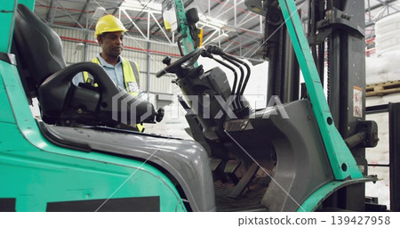 Standing worker wearing yellow helmet hivis vest ID badge by teal forklift site pallets, copy space Standing worker wearing yellow helmet hivis vest ID badge by teal forklift site pallets, copy space 139427958